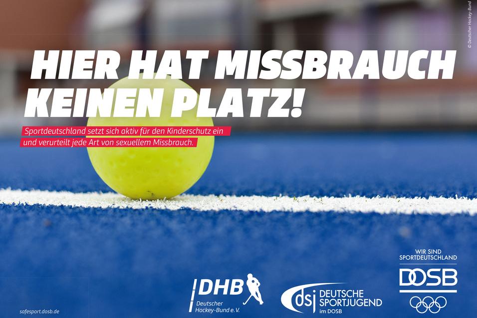 Gelber Hockeyball auf blauem Kunstrasen; Schrift: „Hier hat Missbrauch keinen Platz!“