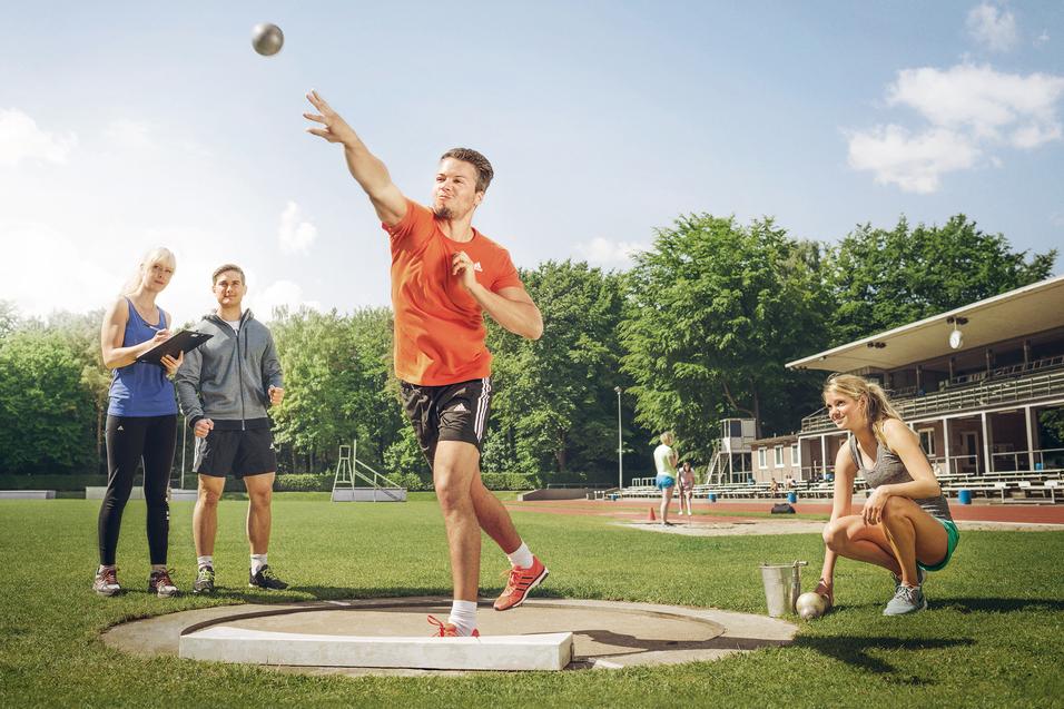 Ein Mann stößt eine Kugel im Stadion, drei Personen beobachten und messen daneben